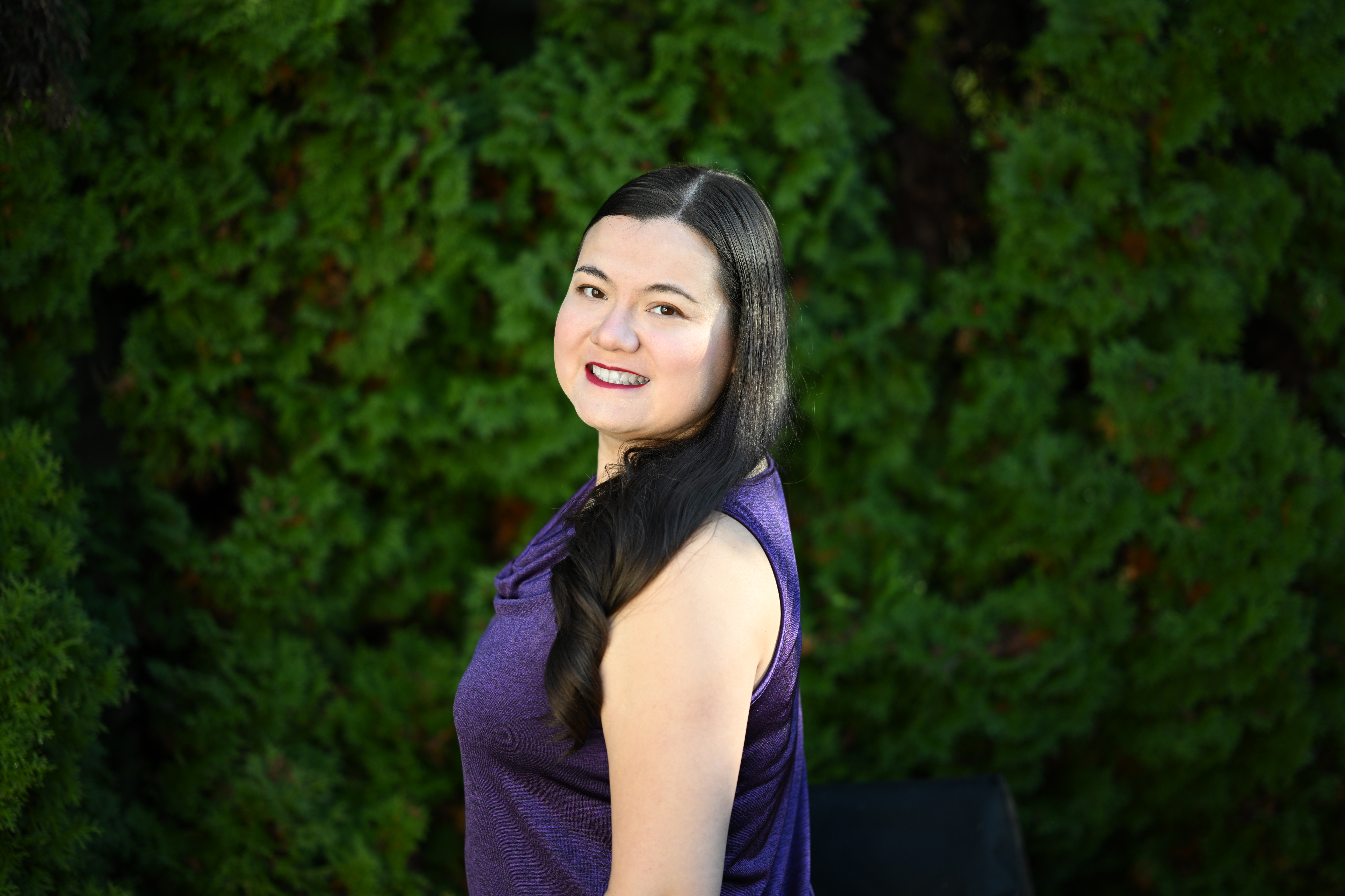 Alt text: Elizabeth wearing a purple shirt with greenery in the background.